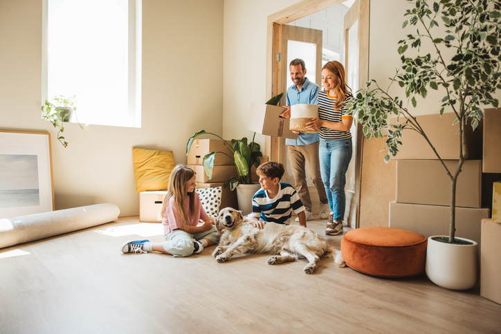 A family with two children and a golden retriever moving boxes into a new home.